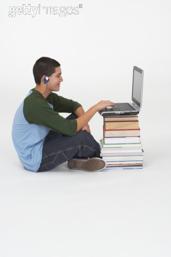 Side profile of a teenage boy sitting in front of a stack of books and using a laptop
